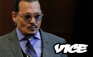 Man in a grey checkered suit, patterned tie, and round sunglasses standing in a courtroom setting with the Vice logo in the corner