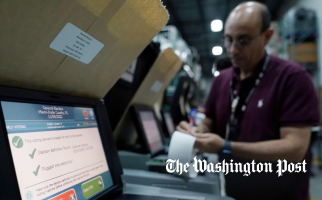 Election worker testing a ballot-scanning machine while examining a printed receipt in a warehouse counting facility