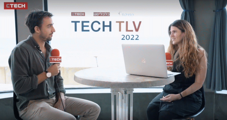 Two interviewers with red CTech microphones sit at a round table with a laptop, TECH TLV 2022 logo displayed behind them