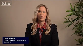 Blonde woman in a black blazer and red patterned shirt speaking on camera with an OurCrowd Virtual Event label and a plant in the background