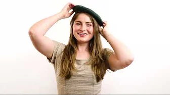 Smiling woman adjusting a green beret against a white background