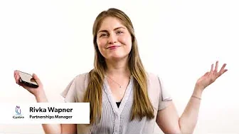 Smiling woman holding a smartphone and making a shrugging gesture against a plain white background with a title card at the bottom left