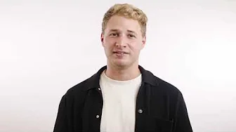 Young blond man wearing a black overshirt and white T-shirt standing against a plain white backdrop