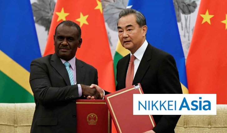 Solomon Islands and Chinese officials shaking hands while exchanging signed documents, flanked by their national flags