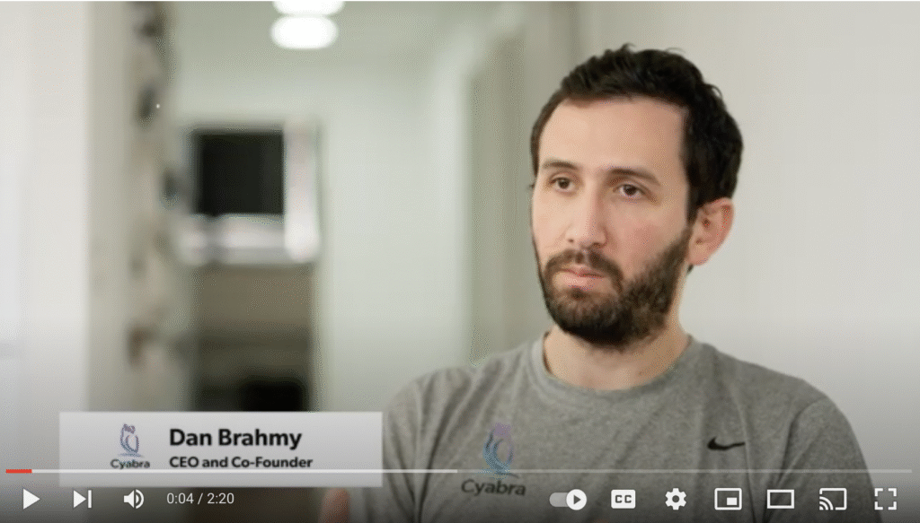Man in a gray Cyabra T-shirt speaking in an office hallway during an interview about online behavior and disinformation