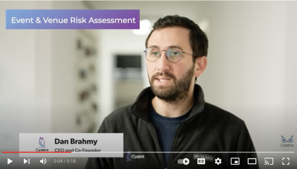 Person with glasses speaking in a hallway; purple banner reads “Event & Venue Risk Assessment” and a lower caption shows their name and title alongside a Cyabra logo