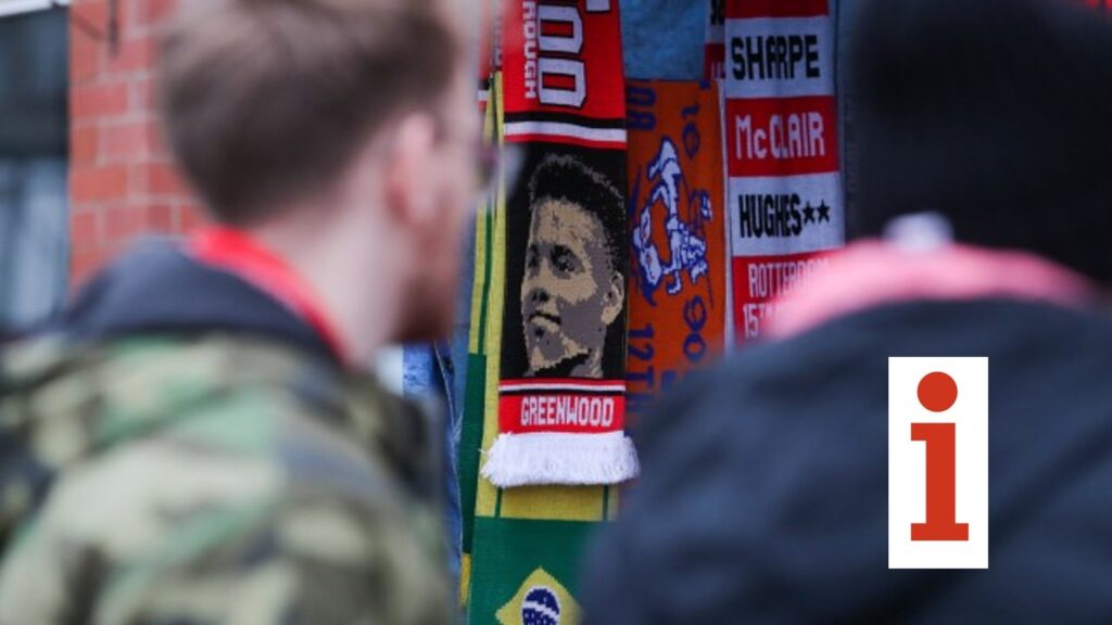 Football fan scarves on display outside a stadium, including one featuring a male player’s portrait, with two people browsing in the foreground