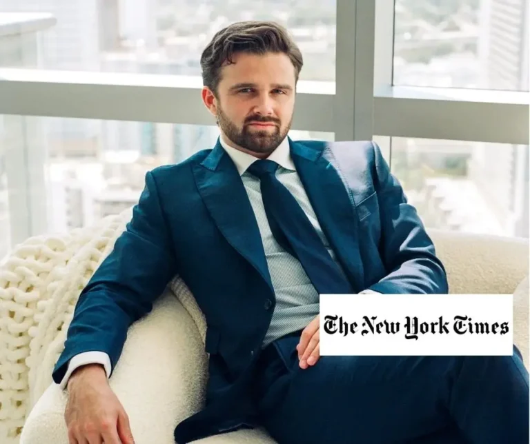 Man in a teal suit sitting on a cream armchair in a high-rise office with city views