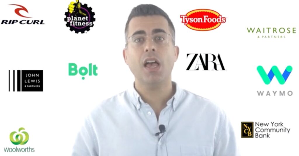Presenter speaking with assorted global brand logos such as Rip Curl, Planet Fitness, Tyson Foods, Waitrose, Zara, Bolt, Waymo, Woolworths, John Lewis, and New York Community Bank surrounding him