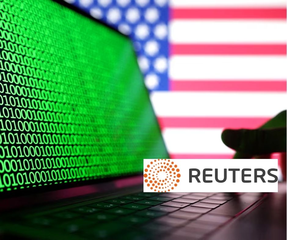 Laptop displaying green binary code with a silhouetted hand on the keyboard and a blurred US flag in the background, representing cyber threats to US elections