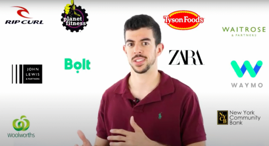 Man in a maroon polo gesturing while surrounded by assorted brand logos such as Rip Curl, Planet Fitness, Tyson Foods, Waitrose, John Lewis & Partners, Bolt, Zara, Waymo, Woolworths, and New York Community Bank