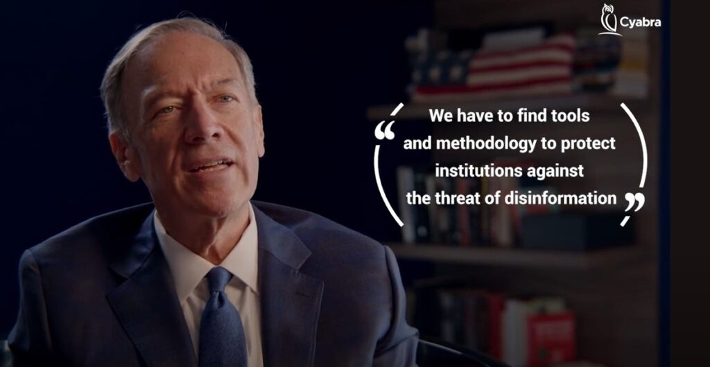 Man in a suit speaking in an interview, with an overlaid quote about finding tools and methodology to protect institutions from disinformation