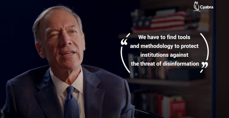 Man in a suit speaking in an interview, with an overlaid quote about finding tools and methodology to protect institutions from disinformation