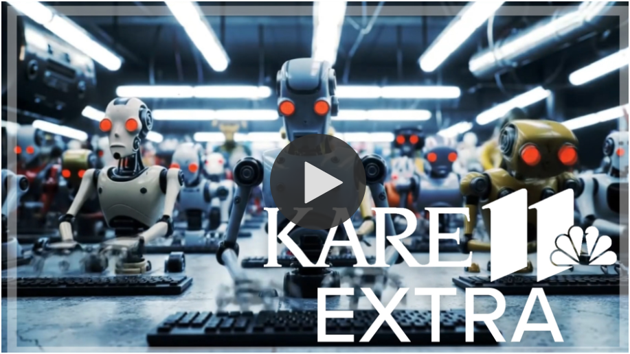 Rows of humanoid robots with red glowing eyes typing at computer keyboards in an industrial setting, KARE 11 Extra logo overlayed