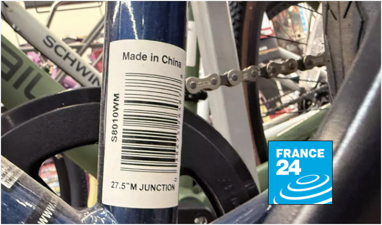Close-up of a bicycle frame bearing a barcode sticker labeled Made in China, with other bikes blurred in the background, illustrating imported consumer goods in the US-China trade debate