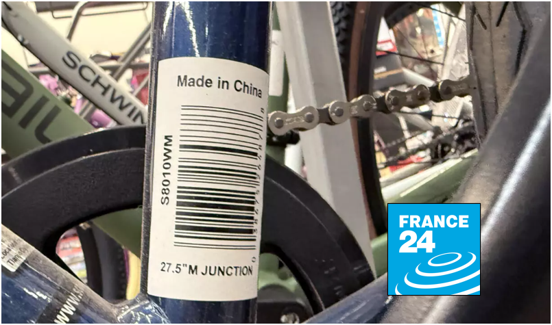 Close-up of a bicycle frame bearing a barcode sticker labeled Made in China, with other bikes blurred in the background, illustrating imported consumer goods in the US-China trade debate