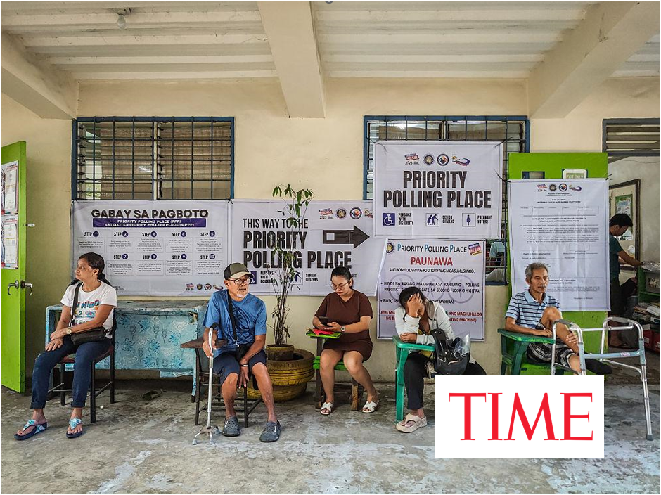 Voters, including elderly people and a man with crutches, sit waiting in a priority polling area in the Philippines, with posters directing to the Priority Polling Place on the wall behind them