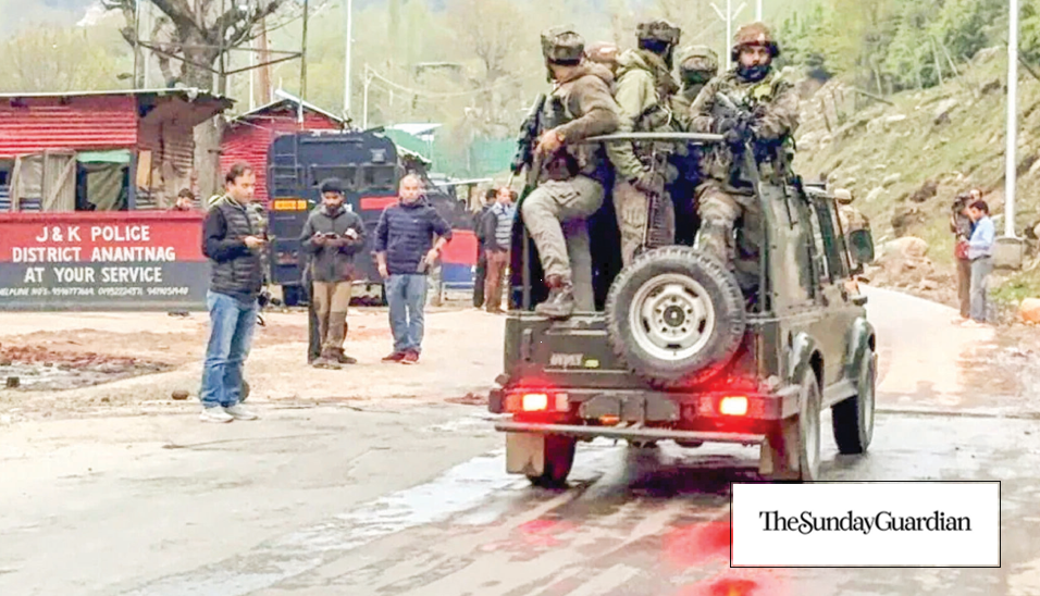 Armed soldiers ride in an open-back jeep past a J&K Police District Anantnag post while civilians and other security personnel stand nearby on a wet mountain road